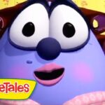Blue, chubby VeggieTales character with large eyes, pink lips, and rosy cheeks smiles in a colorful room; VeggieTales logo bottom-left.