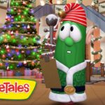 Cartoon cucumber character in a Santa outfit holding a clipboard in a Christmas-lit mall with a decorated tree and presents in the background.