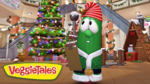 Cartoon cucumber character in a Santa outfit holding a clipboard in a Christmas-lit mall with a decorated tree and presents in the background.