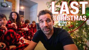 Focused man in a black shirt sits in front of a decorated Christmas tree, with children in red plaid pajamas behind him; bold 'LAST CHRISTMAS' text overlays the scene.