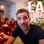 Man in a black t-shirt in the foreground with a Christmas tree; family in red plaid pajamas sits in the background, thumbnail for 'Last Christmas' video.