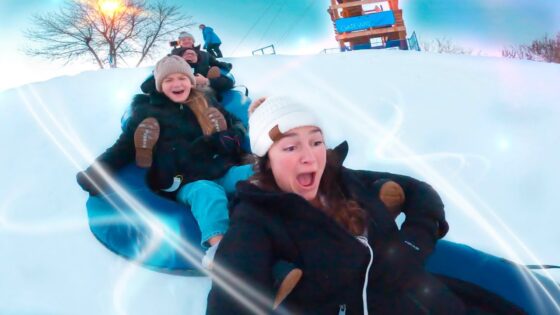 Kids sledding down a snowy hill on a blue inflatable tube, laughing and bundled in winter gear.