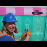 Person wearing a blue hard hat and orange safety vest applying an ice-cream themed vinyl wrap to a teal van with a pink stripe.
