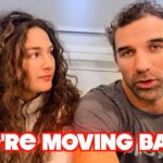 Man and woman sit side by side, looking at each other; bold red caption 'WE'RE MOVING BACK' overlays the bottom, suggesting a video thumbnail about moving back.