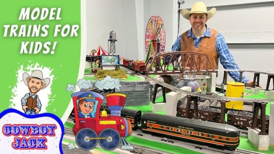 Smiling man in a cowboy hat beside a large model train setup for kids with a green banner reading 'Model Trains for Kids!'