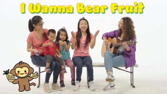 Group of people sitting on a bench: a guitar teacher or performer on the right, singing, with children and a woman, bright text 'I Wanna Bear Fruit' above.