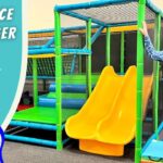 Thumbnail for a video: man in cowboy hat beside a bright indoor playground with yellow double slides and green climbing structures; text reads 'Playplace Scavenger Hunt' and 'Cowboy Jack'