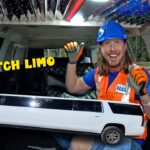 Man in a blue hard hat and orange safety vest holds a large toy stretch limo inside a vehicle, with 'STRETCH LIMO' text.