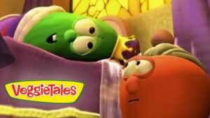 Two VeggieTales characters in a bed scene: a green vegetable lying under a blanket and a red-orange character looking at it as if talking, with a VeggieTales logo visible on the blanket.