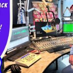 Smiling man in a cowboy hat and vest sits in a radio station studio with mixers and screens; banner reads "Cowboy Jack Visits a Radio Station".