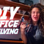 Woman in a workshop holding two cordless drills with bold 'DIY Office Shelving' text overlay on the screen, promoting a DIY tutorial