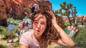 Woman takes a sunny outdoor selfie in a red rock desert, with a group of children playing in the background.