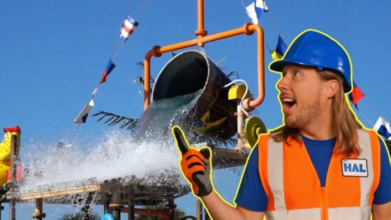 Construction worker in an orange safety vest and blue helmet points at a water splash from a slide or pipe structure behind him.