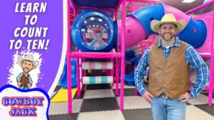 Man in a cowboy hat and vest posing in a colorful indoor playground, with a purple banner that reads 'Learn to Count to Ten!' on the left.