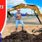 Man in cowboy outfit points at a CAT excavator on a construction site beside dirt piles and a red 'Huge Machines for Kids' banner.
