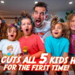 Man with a surprised face surrounded by five kids holding large hair-cutting scissors, indoors, with the bold video title text: 'DAD CUTS ALL 5 KIDS HAIR FOR THE FIRST TIME!' visible across the image