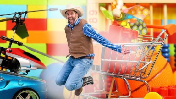 Man in a cowboy hat and vest jumps beside a large toy shopping cart in a colorful playroom.3a8️