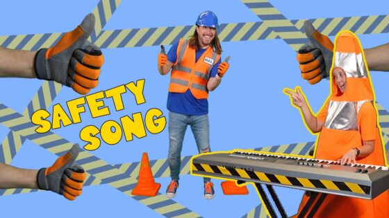 Two people in high-visibility orange safety gear, one at a keyboard and one in a suit, thumbs up with 'SAFETY SONG' on a blue background and construction tape pattern behind them.