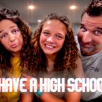 Three friends posing closely indoors, smiling at the camera, with a bold caption across the bottom reading 'WE HAVE A HIGH SCHOOLER'.