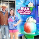 Three people—a man wearing a cowboy hat and vest, and two girls—pose smiling in front of a colorful Sno-Cones truck with a cotton-candy ice-cream sculpture in the foreground