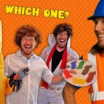 Group of four friends in costumes posing for a game-style photo under the words 'Which One?' a banana costume, a man in a wig, an Elvis-like performer, and a builder with a paint palette smile at the camera on an orange dotted background.