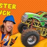 Smiling man in a blue hard hat and orange safety vest beside a bright green monster truck on an orange dotted background with 'MONSTER TRUCK' text above.