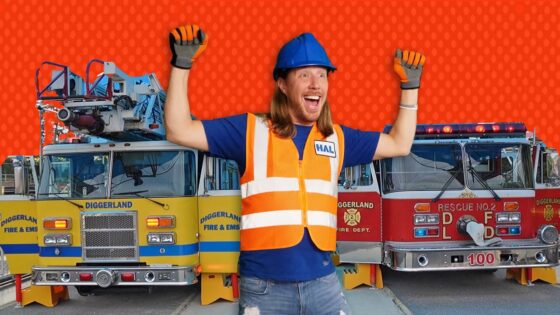 Confident man in a blue hard hat and orange safety vest standing in front of two fire trucks, arms raised in celebration.