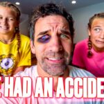 Center-close photo of a man with a bruised eye and purple makeup around it, flanked by two smiling girls in yellow and pink shirts, in a living room; bold caption 'EYE HAD AN ACCIDENT!' across the bottom.