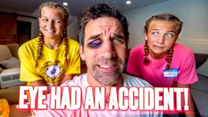 Center-close photo of a man with a bruised eye and purple makeup around it, flanked by two smiling girls in yellow and pink shirts, in a living room; bold caption 'EYE HAD AN ACCIDENT!' across the bottom.