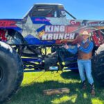 Man in cowboy hat and vest stands next to a giant monster truck named King Krunch on a grassy field.