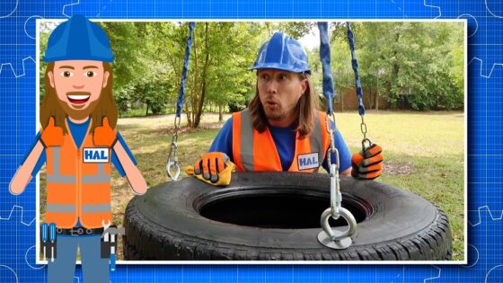 Man in blue hard hat and orange safety vest hoists a tire with a chain in a park; HAL badge visible, with a cartoon HAL character on the left.