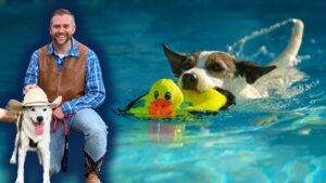 Man in plaid shirt and brown vest sits with a white dog wearing a cowboy hat by a poolside with a leash