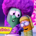 Two VeggieTales characters perform on a colorful stage, singing into microphones with a drum set in the background and the VeggieTales logo visible in the corner.