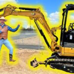 Man in a cowboy hat and vest poses beside a yellow CAT excavator on a construction site.
