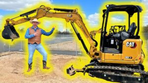 Man in a cowboy hat and vest poses beside a yellow CAT excavator on a construction site.