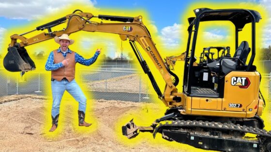 Man in a cowboy hat and vest poses beside a yellow CAT excavator on a construction site.