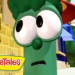 Green VeggieTales character with oversized eyes wearing a Santa hat, against a yellow brick backdrop.
