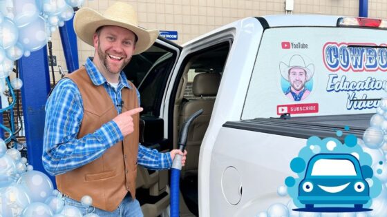 Smiling man in a cowboy hat and brown vest points at a white van door, holding a blue vacuum hose beside a festive setup.