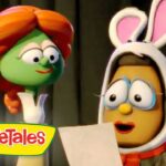 Two VeggieTales characters on a stage: a green vegetable with orange hair speaks to a brown character wearing bunny ears, holding a sheet of paper. Logo reads VeggieTales in the corner.