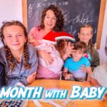A mom sits with six children around a wooden table, holding a newborn baby; chalkboard and shelves behind, with bold '1st Month with Baby #6' text overlay indicating a YouTube thumbnail.