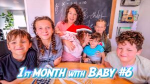 A mom sits with six children around a wooden table, holding a newborn baby; chalkboard and shelves behind, with bold '1st Month with Baby #6' text overlay indicating a YouTube thumbnail.