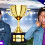 Two people in denim jackets stand beside a large gold trophy on a stadium set; banner says Exclusive and Full Episode, suggesting a world record video thumbnail.
