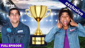 Two people in denim jackets stand beside a large gold trophy on a stadium set; banner says Exclusive and Full Episode, suggesting a world record video thumbnail.