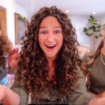 Three people with curly hair smiling at the camera in a bright living room.