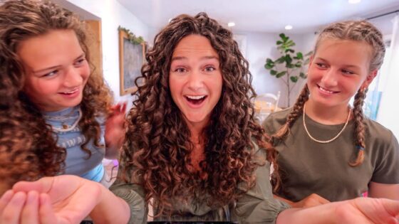 Three people with curly hair smiling at the camera in a bright living room.