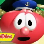 Close-up of a red VeggieTales character with a sailor's hat, wide eyes, and open mouth, set against a sandy scene with the VeggieTales logo in the corner.