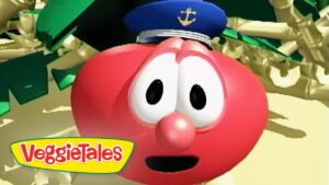 Close-up of a red VeggieTales character with a sailor's hat, wide eyes, and open mouth, set against a sandy scene with the VeggieTales logo in the corner.