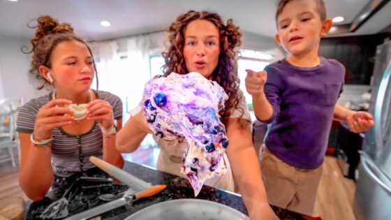 Three people gather around a kitchen counter, holding a colorful purple-blue ice sculpture head they made together.