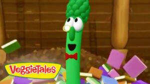 Green cucumber character from VeggieTales with a red bow tie, smiling in a colorful block-filled scene (logo bottom-left).