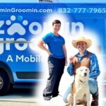 Blue mobile pet grooming van with two staff and a dog in front; large 'ZoominGroomin' branding and phone number on the side.